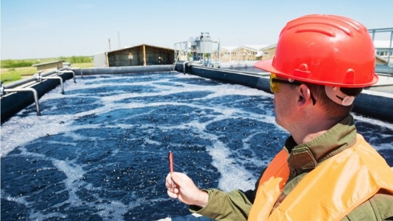 Engineer in the foreground standing in front of a wastewater treatment plant.