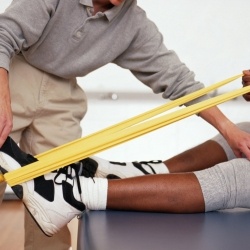 Physical Therapist is holding the foot of a patient while they are using a tension band.