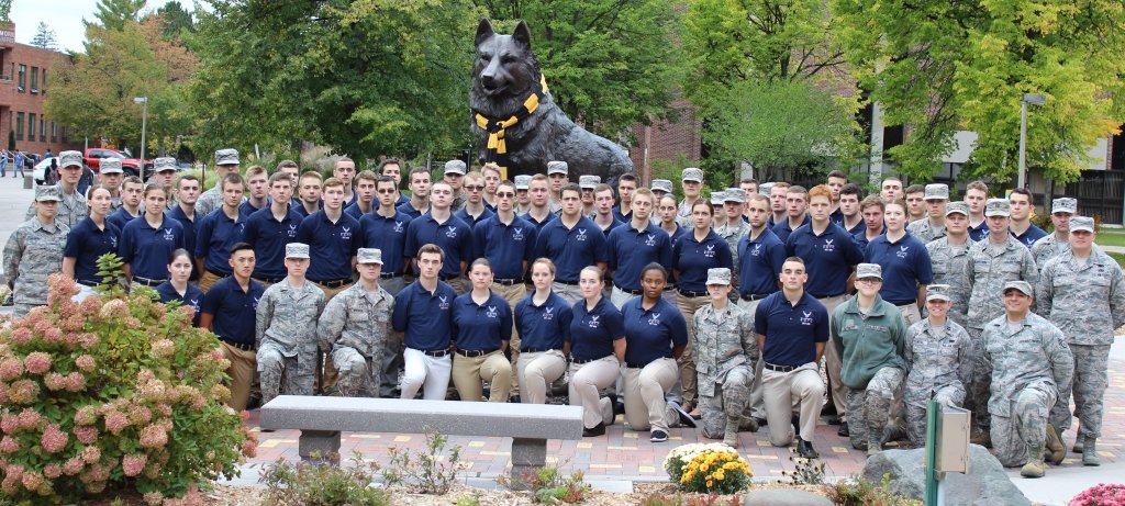 Air Force ROTC students in fatigues with officers in kahkis and polo shirt with AFROTC logo standing in front of the Michigan Tech Husky statue.