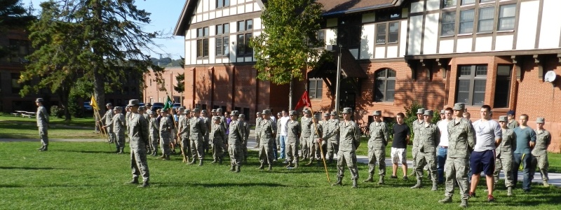 Cadets in uniform and high school students in plain clothing standing attention outside the ROTC building