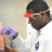 A man pouring chemicals in a lab coat and goggles