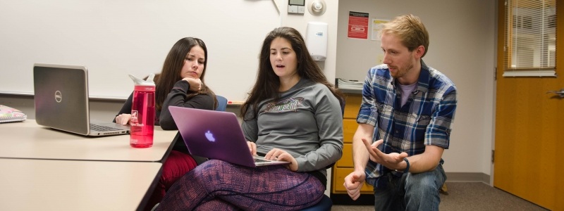 Three students sitting together with a laptop discussing.
