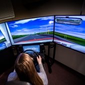 A students sits at a driving simulator with three screens