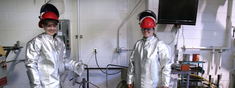 Engineering students standing near high heat research equipment while wearing safety equipment.