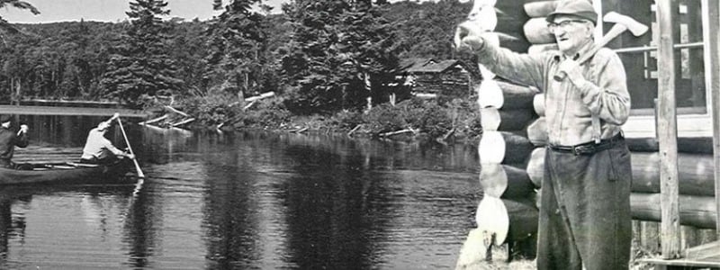 Black and white photo of people with an axe and canoeing.