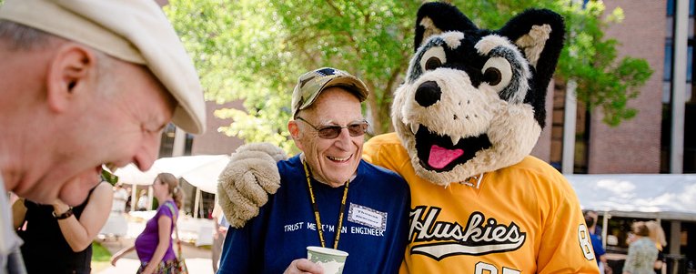 Alumnus standing with Blizzard T. Husky at reunion.