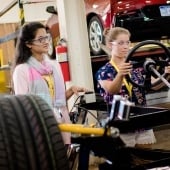 Two women work on a car in a lab.