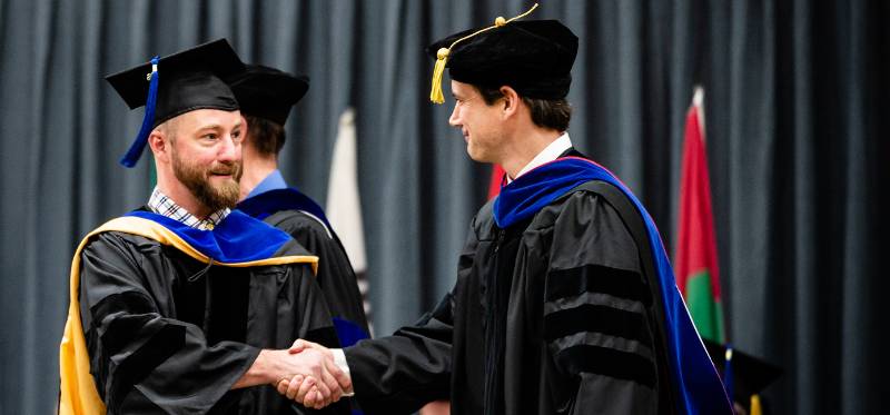 Graduate faculty shaking hands with graduating student