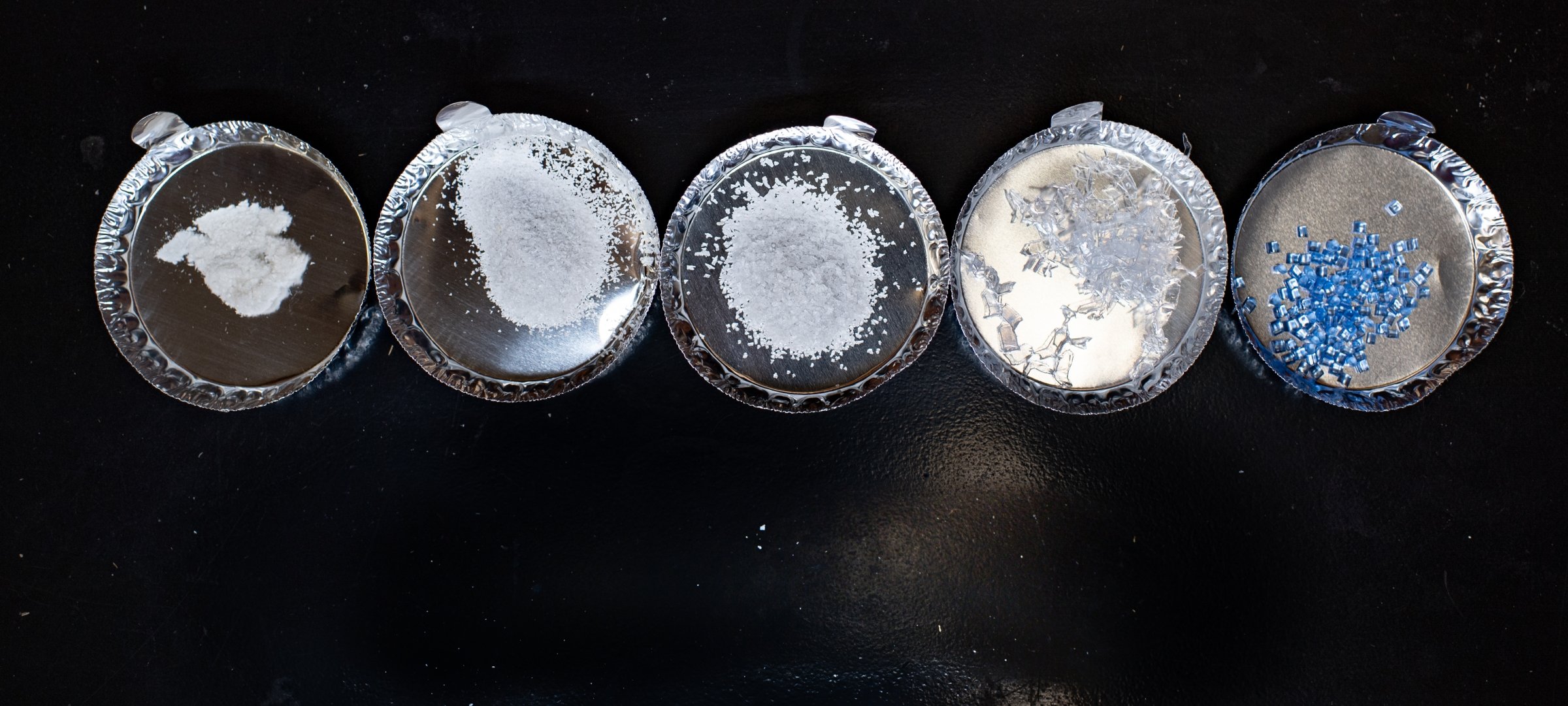 Varying sizes of plastic fragments in five different petri dishes on a countertop.