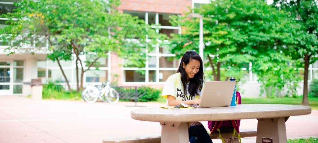 Student sitting outside at a table with a laptop.