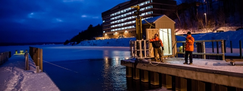 Two researchers using dock equipment during a cloudy winter evening on the dock of the GLRC