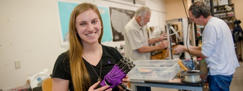 Female student in a lab holding a prosthetic hand.