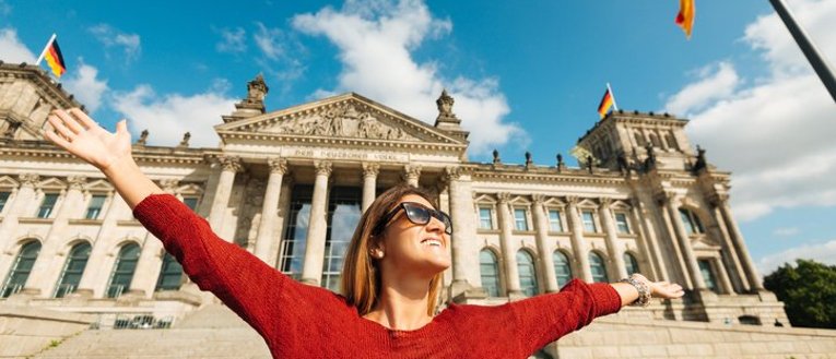 Woman standing in front of a old German Building with arms outstretched, smiling.