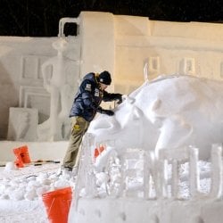 student works at night on a snow statue at winter carnival