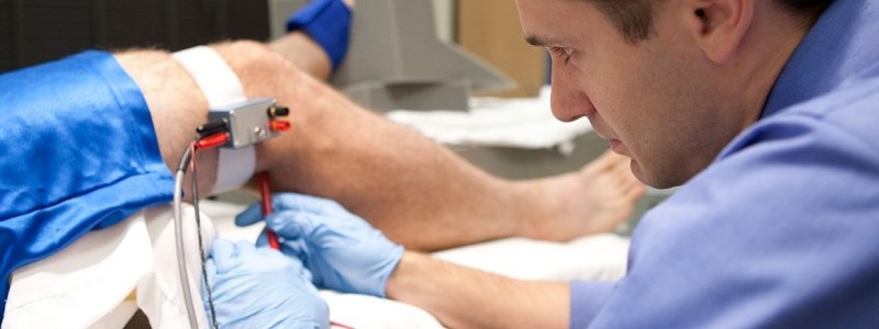 Dr. Jason Carter adjusts red and black wires connected to a device on a participants knee