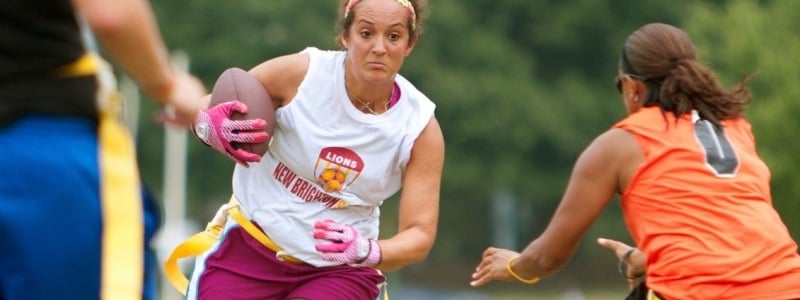 Woman running with football while another attempts to grab her flag during flag football.