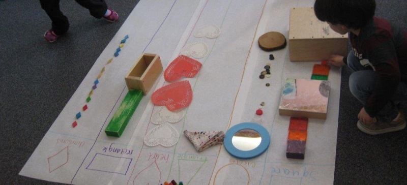 Child sorting objects onto large paper by shape.