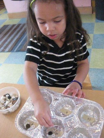 Child counting buttons into spaces in a muffin tin.