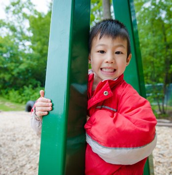 Child standing outside next to the green swing structure.