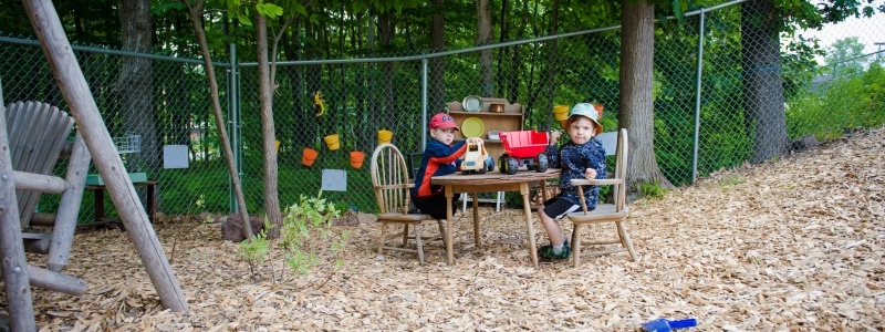 Two boys playing with trucks at a table outside.