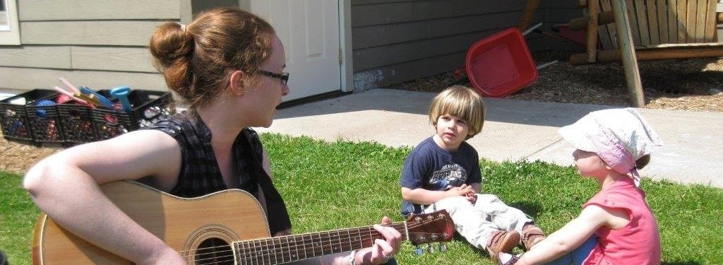 Teacher playing the guitar outside with two children.