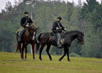 Two people dressed in old military uniforms on horseback.