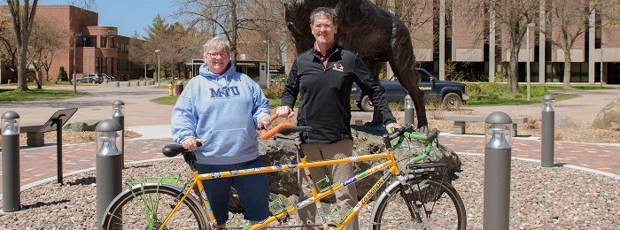 Jim '81 (Civil Engineering) and Shawn '82 (Computer Science) Rathbun with their tandem bicycle in front of the husky statue.