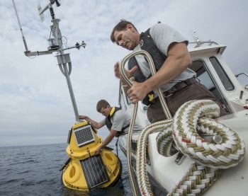 Two people deploying a buoy from a boat.