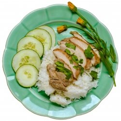 Chicken on a bed of rice with cucumbers and dandelions on the side.