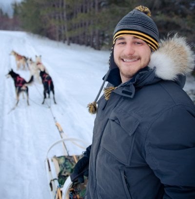 Adam Schmidt on a sled with dogs harnessed up.