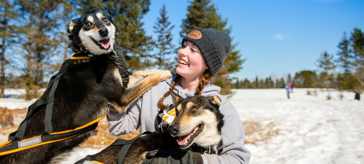 Student hugging and petting two sled dogs.