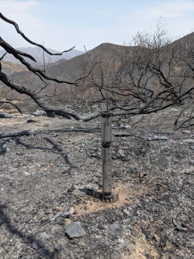 A soil infiltrometer on recently burnt soil with a burnt forest in the background.