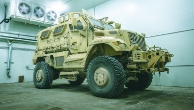 Large armored vehicle in a room with fans blowing cold air.