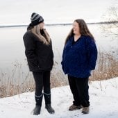 Two laughing women stand next to an icy Keweenaw Bay