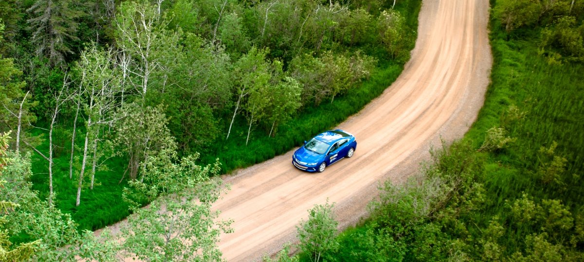 Blue car driving on a dirt road through the forest.