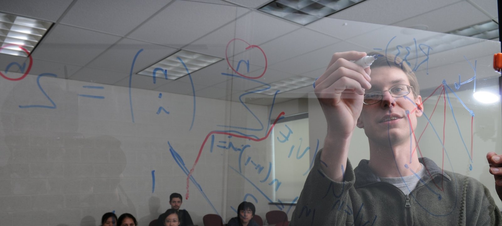 Mathematician writing out equations on a glass board.