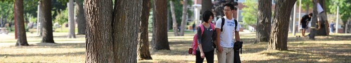 A young couple walking between trees on campus