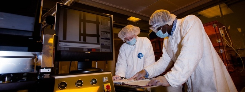 Two researchers in full protective gear look over notes in a binder inside the Microfabrication lab