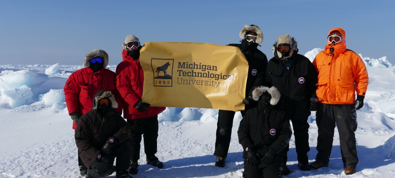 MTRI Scientists working on an arctic sensing project and holding a Michigan Tech banner near Barrow, AK