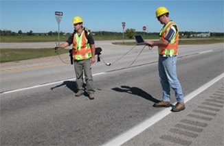 Two people using equipment on a road.