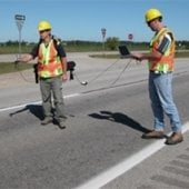 Two people taking measurements on a road.