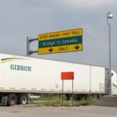 Semi truck driving under Bridge to Canada sign.