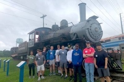 Group of males outside near an older engine.