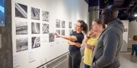 Three gallery attendees observe a collection of nine black and white microscopic images in the Rozsa’s A-Gallery.