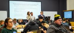 Three students share their SMART goals on a projection screen behind them as other students in the class look on.