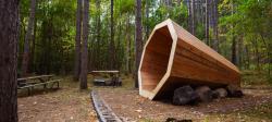 A large conical, megaphone shaped, wooden structure in the woods.