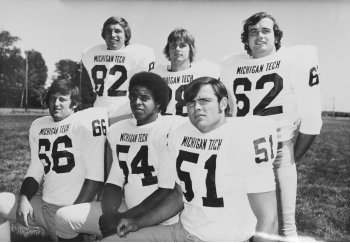 Six football players wearing Michigan Tech jerseys on a football field
