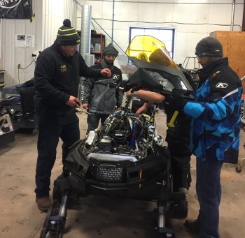 Students gather around a snowmobile to put the outside casing back on it.