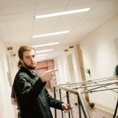 young man with a beard pointing at steel tubing in a hall