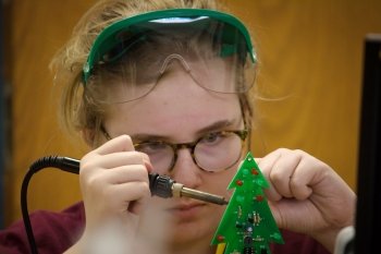 A young woman concentrates on making a circuit board that is green